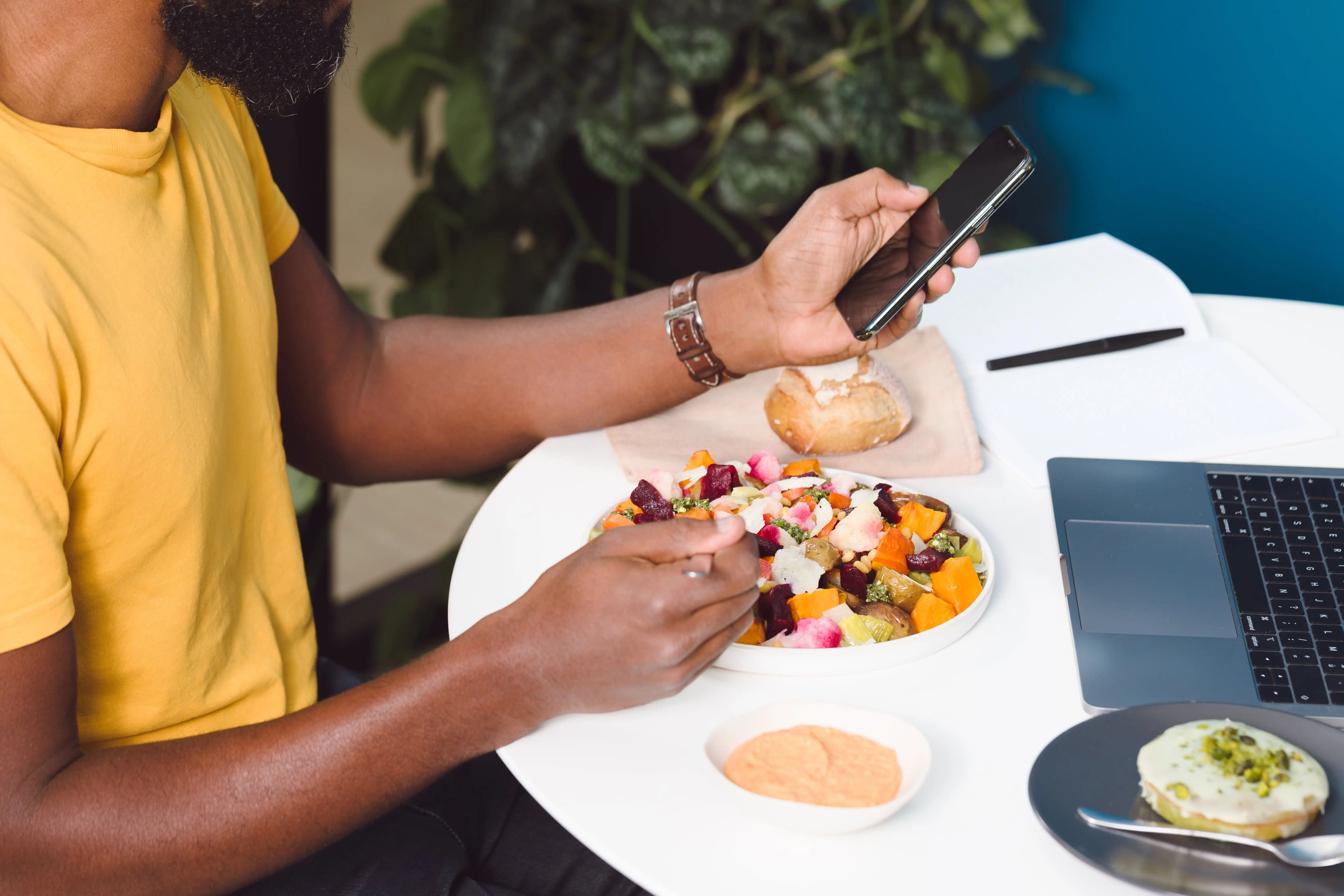L'importance d'une alimentation saine au travail pour le bien-être des salariés. Un employé mange son plat au bureau devant son ordinateur et tien son téléphone dans la main.